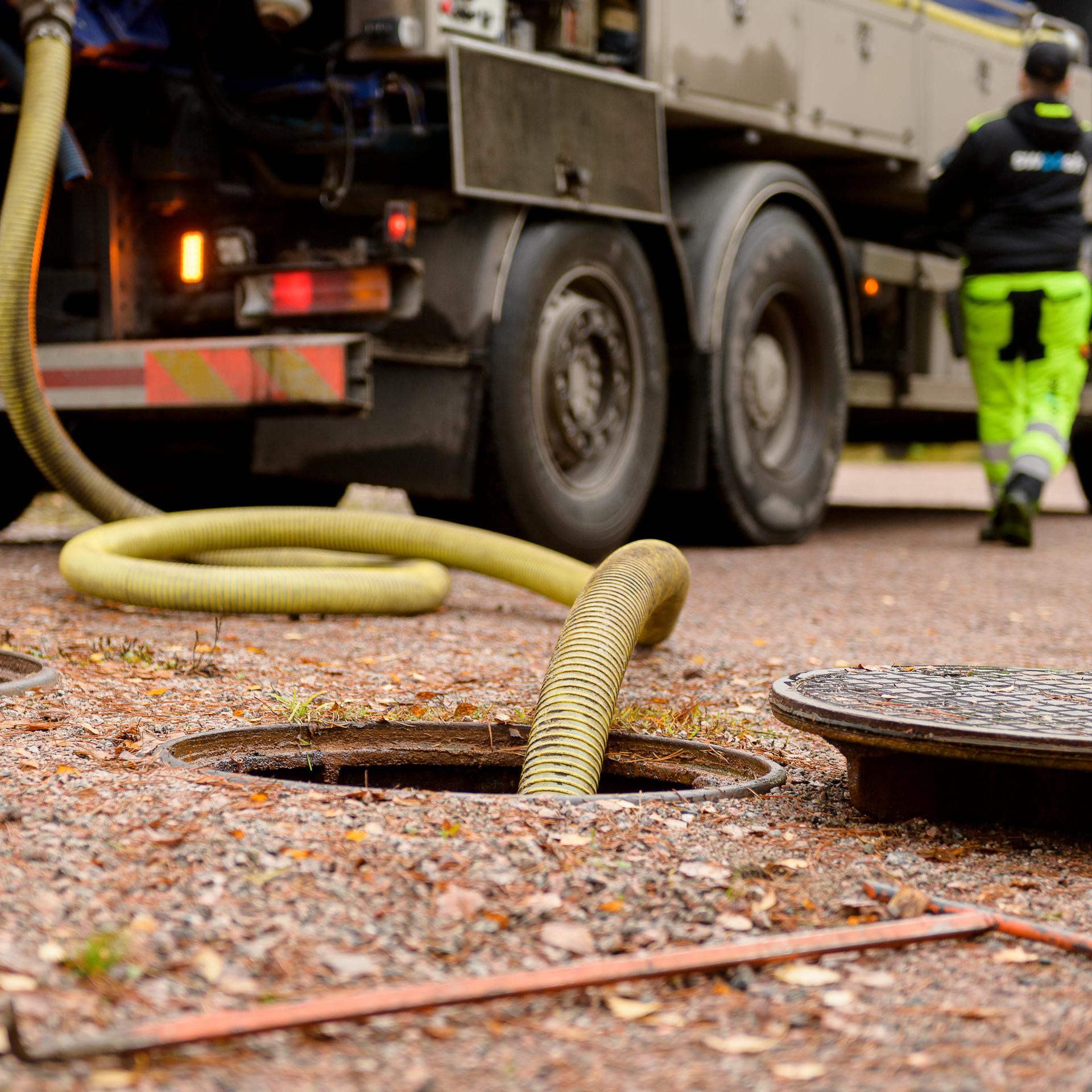 Lång gul slang nedstoppad i brunn och ett brunnslock på sidan om
