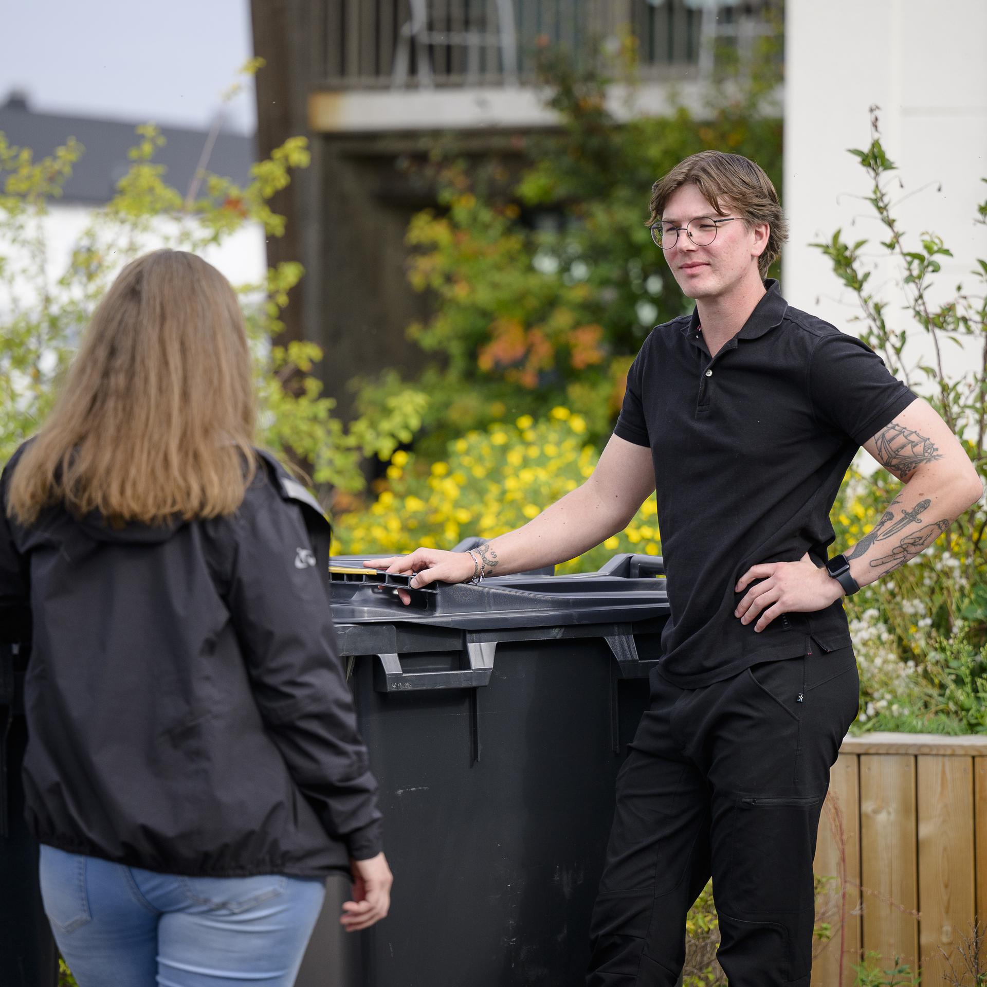 Man står står med hand på ett sopkärl och pratar med en kvinna