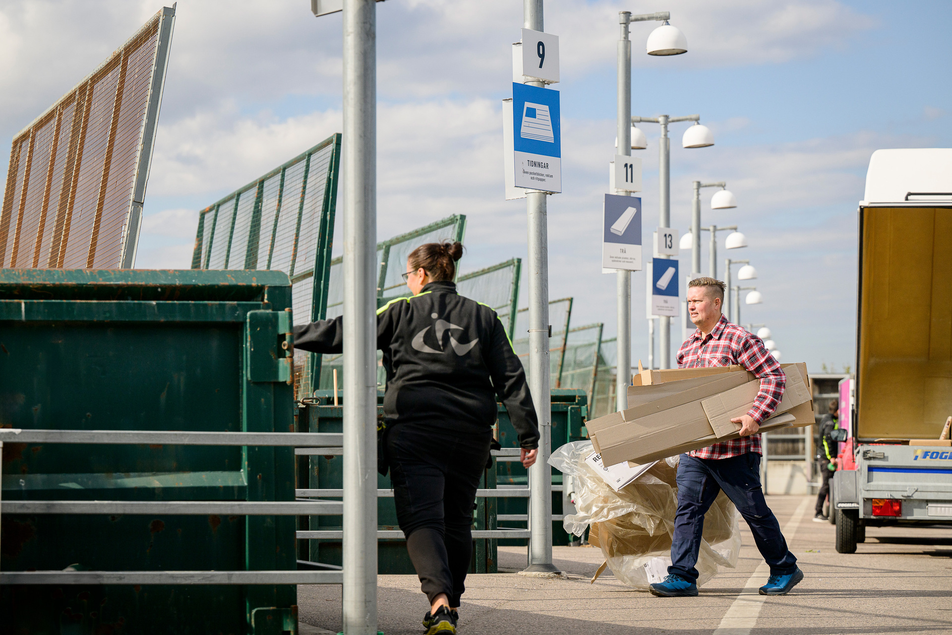 Kvinna med återvinningssymbol på ryggen pekar mot container och man håller en bunt wellkartonger under armen